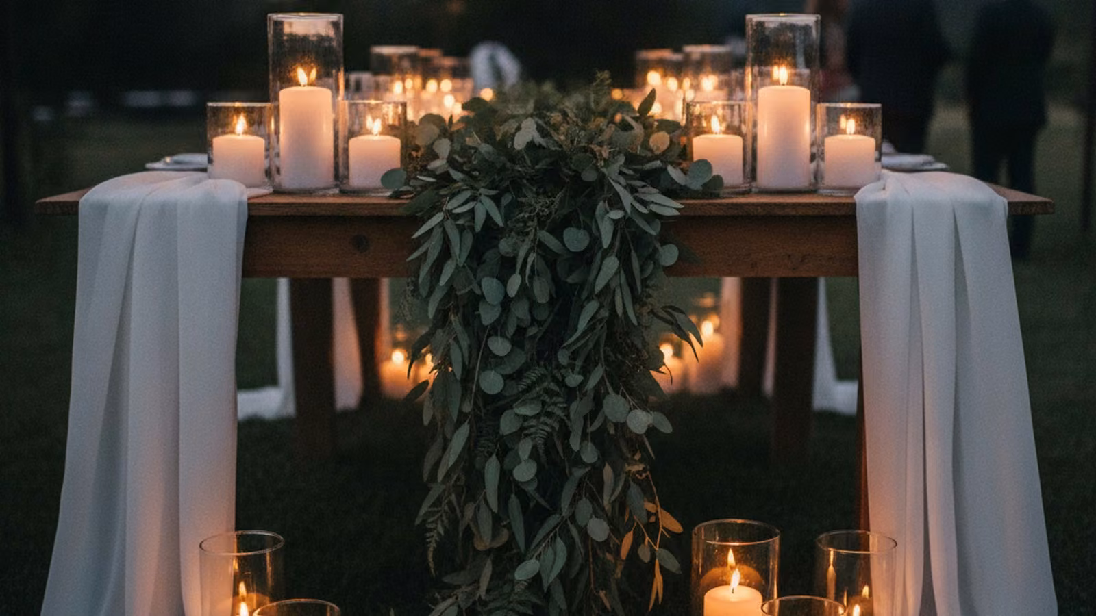 Greenery table runner with candles on a long wooden event table at dusk