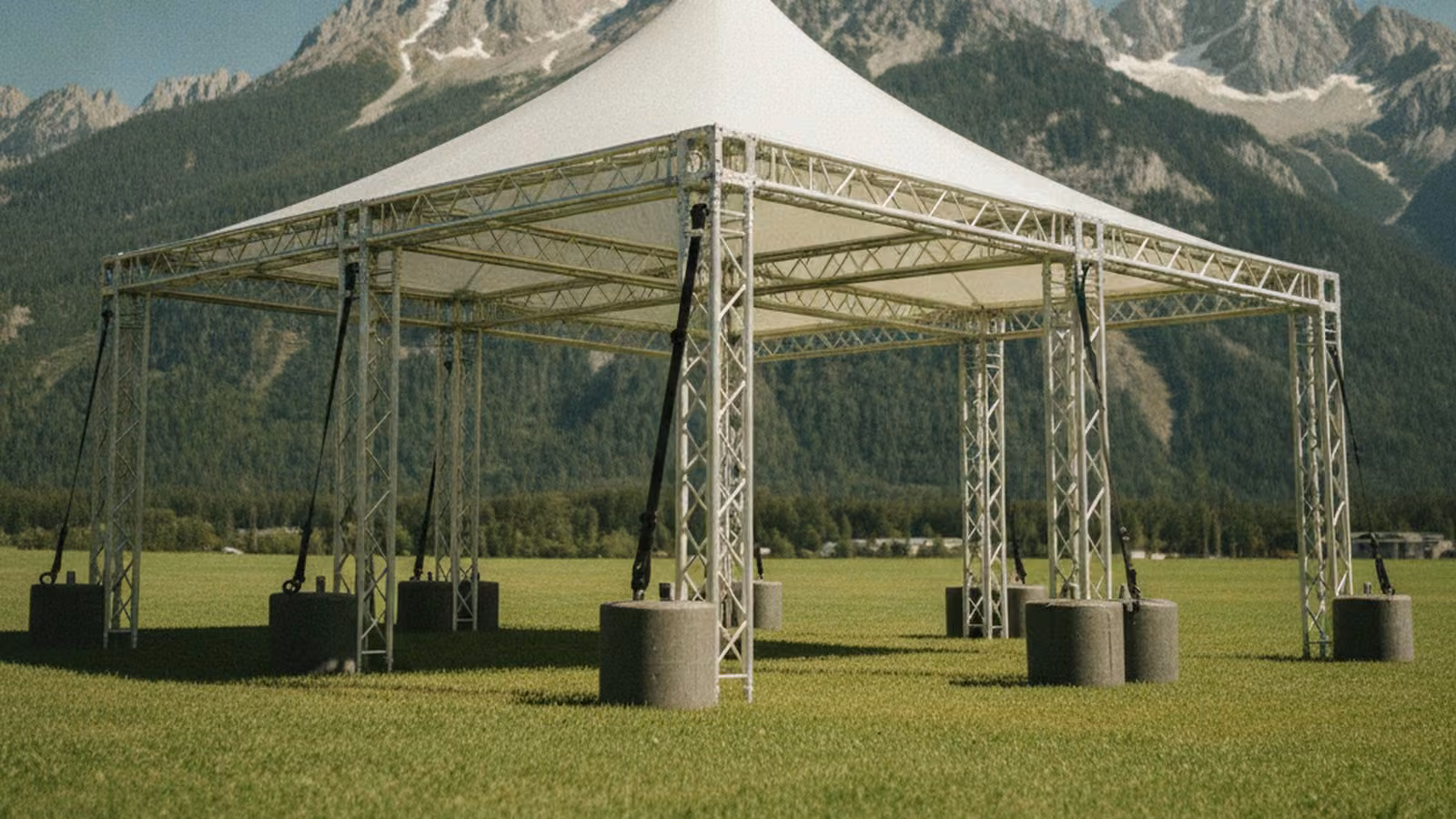 A framed event tent ballasted on open ground below a steep mountain range