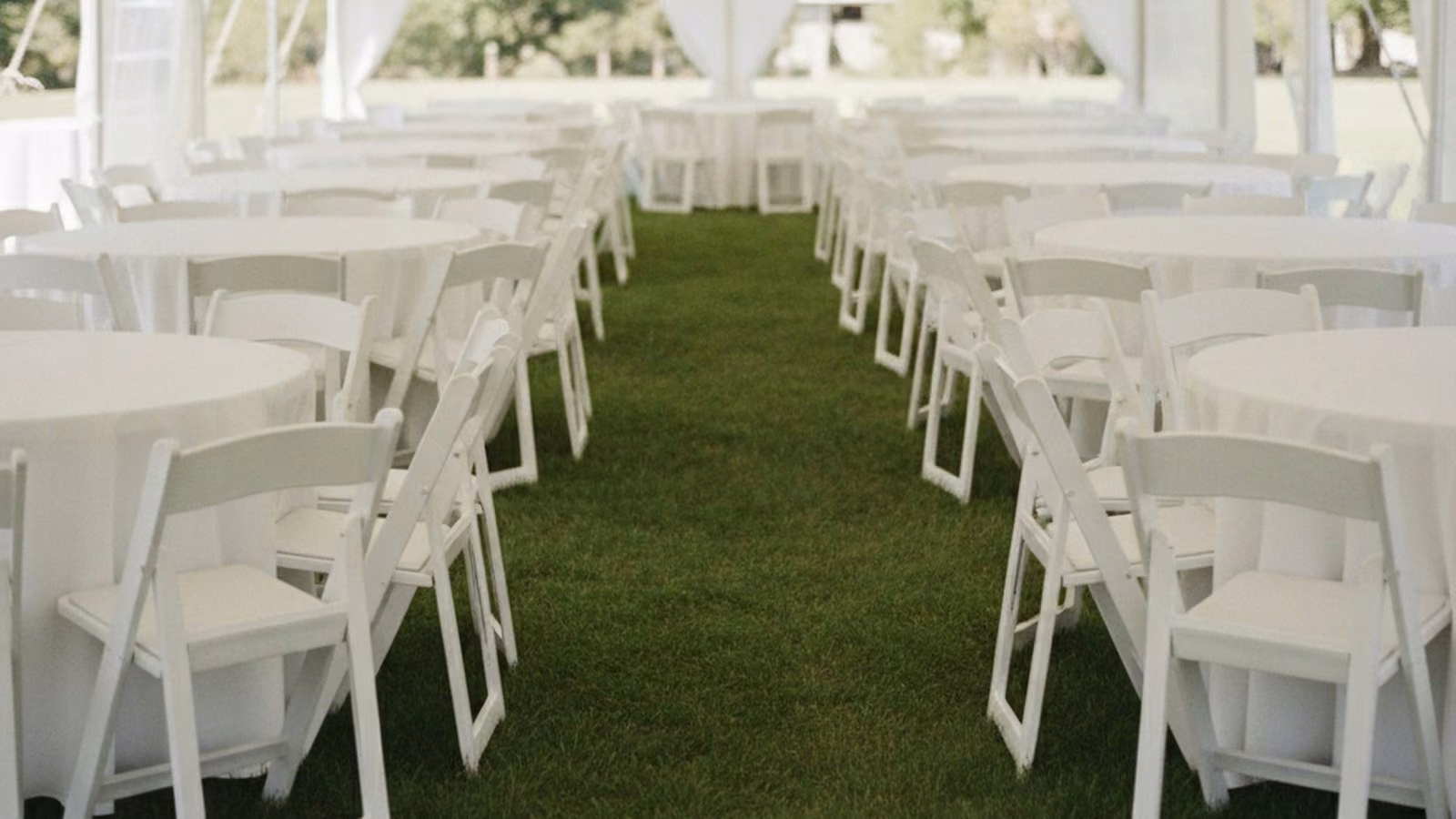 Rows of white folding chairs and round tables under an event tent